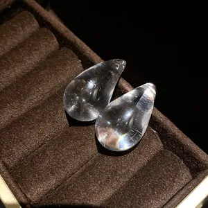 Macro detail of transparent water-drop earrings on a luxury brown velvet display