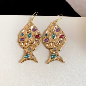 Orecchini a pesce dorati alla moda con strass colorati e texture metallica rugosa.