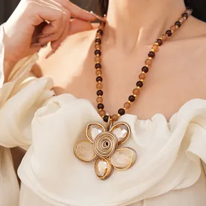 Gros plan d'un collier pendentif fleur perlé élégant porté sur un haut à volants crème