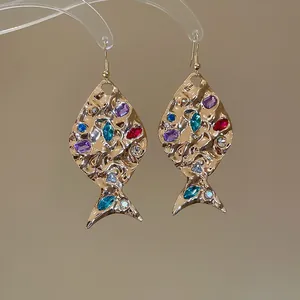 Primo piano di orecchini a forma di pesce color oro con strass colorati brillanti.