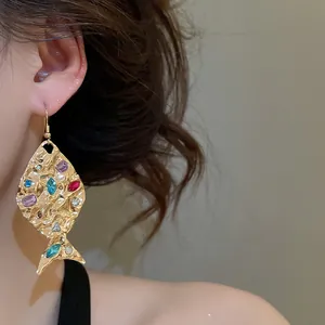 Primo piano di orecchini a forma di pesce d'oro con strass colorati e trama stropicciata.