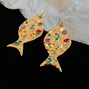 Dettaglio di orecchini a pesce d'oro con texture pieghettata e strass colorati scintillanti
