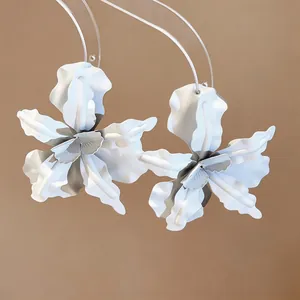 Macro detail of white spray-painted flower stud earrings on minimalist background
