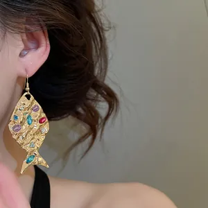 Primo piano orecchino a pesce dorato con strass colorati e trama stropicciata.