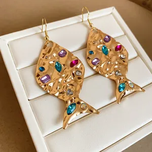 Primo piano di orecchini a forma di pesce in oro martellato con cristalli colorati.
