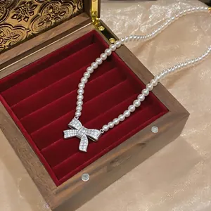 Detailed view of a bow pearl necklace displayed in a luxury red velvet jewelry box.