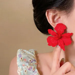 Detailed close-up view of an oversized matte red flower stud earring worn on a model's ear