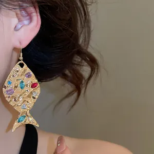 Dettaglio dell'orecchino a pesce dorato con strass colorati e trama stropicciata.