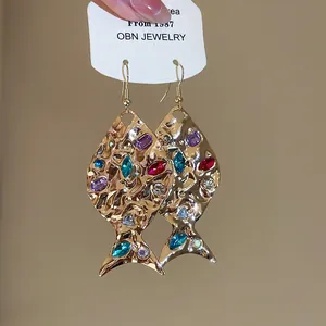 Primo piano di orecchini a amo a forma di pesce d'oro con strass colorati e metallo.