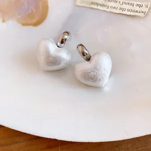 Dettaglio di eleganti orecchini di perla a forma di cuore su uno sfondo di conchiglia iridescente.