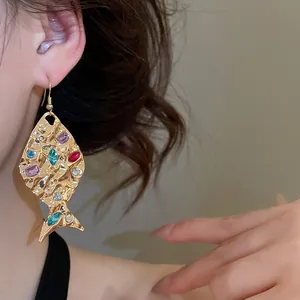 Elegante orecchino a goccia in oro a forma di pesce con strass colorati indossato da modello