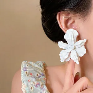 Detailed view of oversized white spray-painted floral earring worn on ear for scale