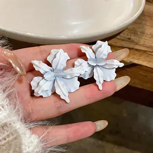 Close-up view of oversized matte white orchid flower stud earrings held in a hand