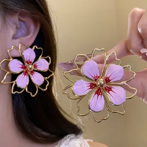 Macro detail of oversized pink enamel flower earrings with gold hollow frame outline