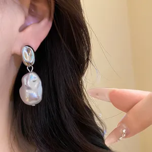 Close-up of retro silver pea stud earrings with baroque pearl pendants on ear.