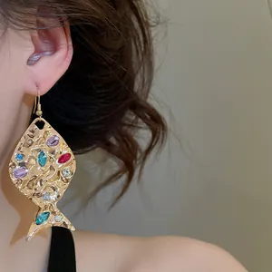 Vista dettagliata di un orecchino a forma di pesce dorato con strass colorati su modella