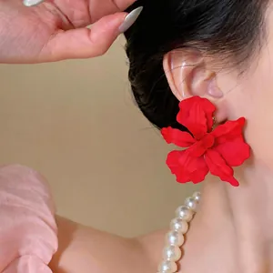 Detailed close-up of vibrant red matte painted flower stud earrings worn by a model