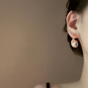 Primo piano di un elegante orecchino a C dorato con pendente in resina rosa sull'orecchio.