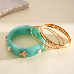 Close-up of a 4-piece teal resin and golden metal bangle set with starfish and faux pearls