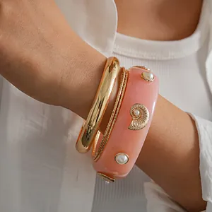Detailed view of pink resin shell bracelet and gold bangles set for vacation wear