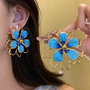 Macro view showing the glossy blue enamel and gold details of these flower earrings