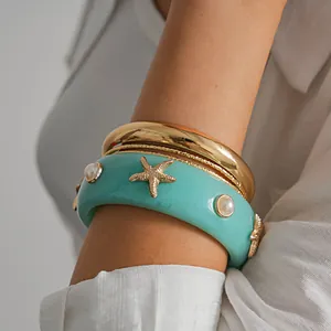 Close-up detail of resort style stacked gold and turquoise resin starfish bangles with pearls