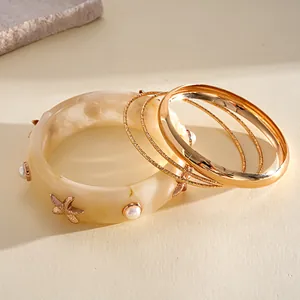 Close-up of bohemian resin starfish bangle and gold bracelets set with pearl accents