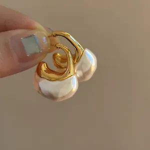 Dettaglio di orecchini a forma di C color oro con pendenti in resina perlata strutturata.