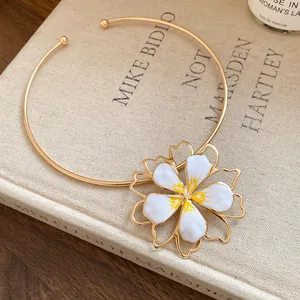 Detail view of a gold-toned flower choker with white enamel petals on a vintage book.