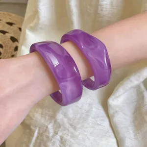 Nahaufnahme von zwei lila marmorierten Acrylarmreifen an einem schlanken Handgelenk
