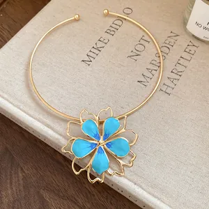 Elegant gold-toned choker featuring a blue enamel flower pendant on a vintage book.