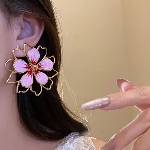 Close-up of a large pink enamel flower earring worn by a model with golden frames