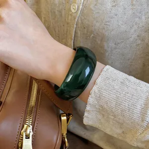 Nahaufnahme eines grünen marmorierten Acryl-Armreifs am Handgelenk mit brauner Tasche.