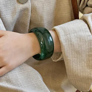 Nahaufnahme eines tiefgrünen, marmorierten Acryl-Armreifs am Handgelenk mit Textur.