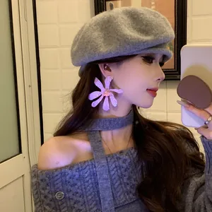 Close-up detail of stylish oversized purple flower earrings worn with a trendy gray beret.