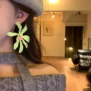 Close-up detail of large lime green floral earrings worn by a model in a cozy indoor setting