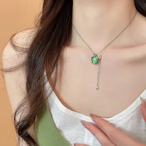 Dettaglio di una collana con ciondolo a uva verde chiaro e piccolo fiore su una modella