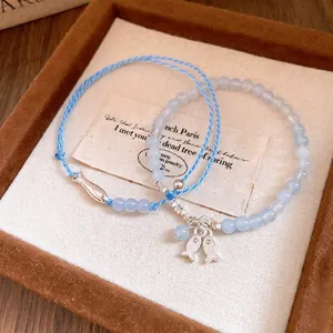 Exquisito juego de pulseras de cuerda azul y cuentas con dijes de peces plateados.