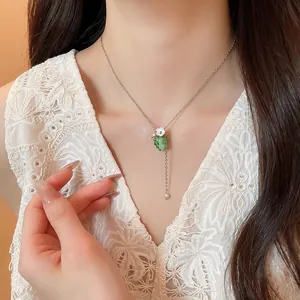 Primo piano di una delicata collana con ciondolo a uva verde su modella in abito di pizzo