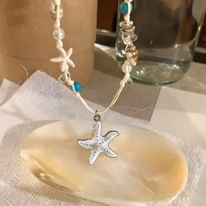 Detailed view of a white enamel starfish pendant on a woven beaded shell necklace