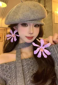 Detailed view of oversized purple flower earrings worn with a chic grey beret