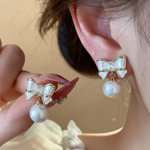 Elegante Schleifen-Ohrringe mit Perlenanhänger, 14K vergoldet, Detailansicht am Ohr.