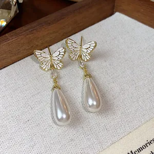 Detail von vergoldeten Schmetterlingsohrringen mit eleganten weißen Tropfenperlen