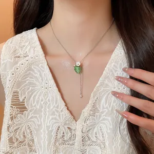 Dettaglio di una collana con ciondolo a uva verde traslucido e fiore bianco.