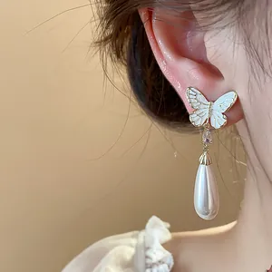 Nahaufnahme eleganter, 14 Karat vergoldeter Schmetterlingsohrringe mit Perlenanhängern.