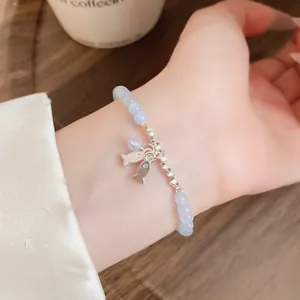 Detalle de una pulsera de cuentas de piedra azul claro con delicados peces plateados