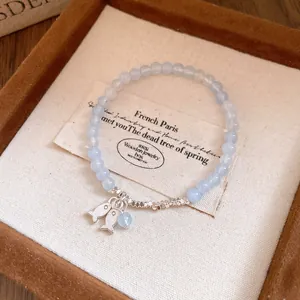 Primer plano de una pulsera de cuentas de piedra azul con dijes de peces plateados
