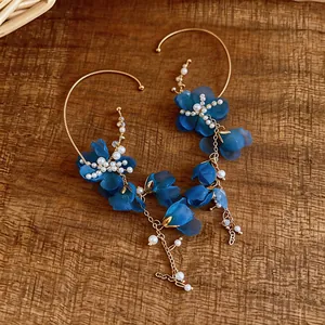 Detailed view of ethereal blue fabric flower and pearl ear cuffs on a wooden background