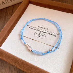 Detalle exquisito de una pulsera de cordón trenzado azul con pez plateado y cuentas.