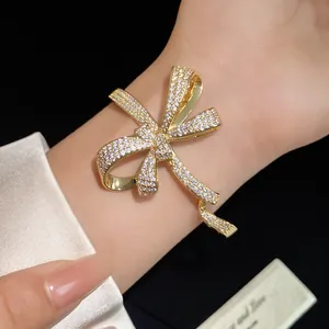 Close-up detail of a sparkling zircon-inlaid gold bow bracelet on a wrist